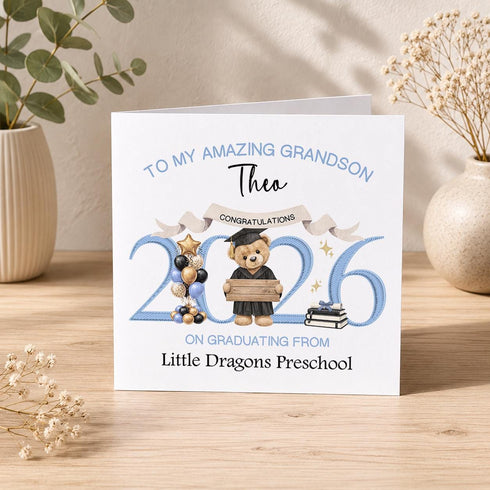 Personalised preschool graduation card with blue year numbers, graduate teddy bear, balloons, books and custom nursery wording.