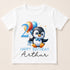 A white t-shirt with a cartoon penguin holding balloons and the number "2" on it, along with the text "Happy Birthday Arthur".