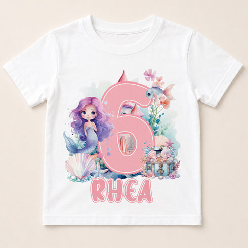 A white t-shirt with a mermaid and underwater theme, featuring the number 6 and the name "Rhea" printed on it.