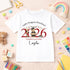White children’s T-shirt featuring a personalised red 2026 teddy bear preschool graduation design, photographed with colourful nursery and craft accessories.
