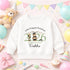 White children’s sweatshirt with a personalised green 2026 teddy bear nursery graduation design, displayed with colourful balloons, bunting and party decorations.