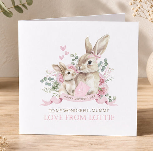 A greeting card featuring a mother rabbit and her baby rabbit, surrounded by pink flowers and greenery, with the text "Happy Mother's Day" and "To my wonderful mummy, love from Lottie" printed on it.
