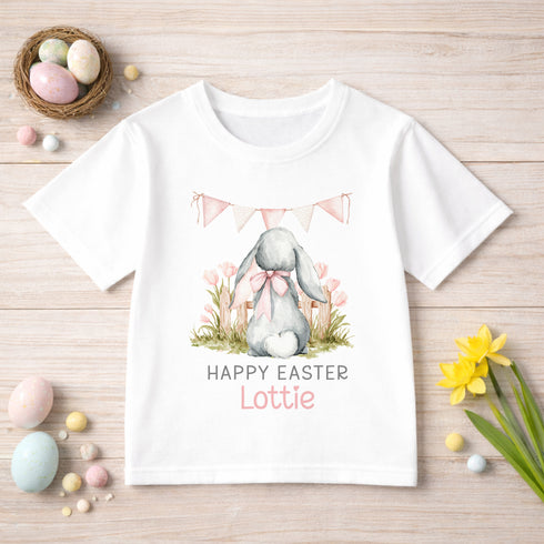 A white t-shirt with a bunny graphic and the text "Happy Easter Lottie" printed on it, along with Easter decorations such as a basket of eggs, flowers, and a banner.
