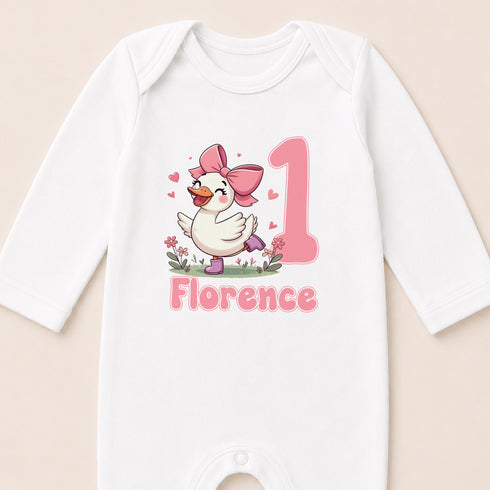 A white onesie with a cartoon image of a duck wearing a pink bow and the number 1, along with the name 'Florence' printed below.