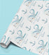 a roll of wrapping paper with a repeating pattern of blue whale illustrations and anchors.