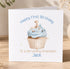 A white greeting card with a cupcake illustration and the text "Happy First Birthday To a scrummy Grandson Jack" printed on it.