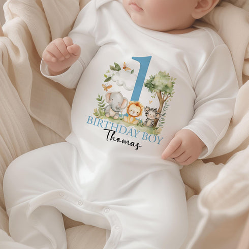 Personalised 1st birthday boy outfit with blue number 1, safari animals, elephant, lion, zebra, tree and custom name, shown on bib, vest, sleepsuit, t-shirt and white pyjamas.