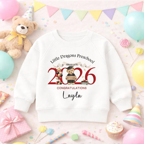 White children’s preschool graduation sweatshirt with a personalised red 2026 teddy bear graduate design, preschool name and child’s name on a pastel party background.