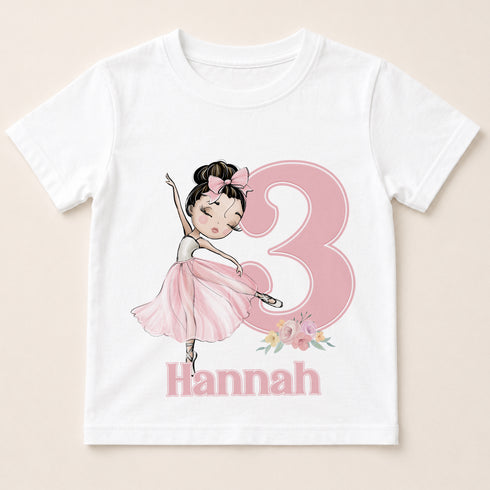 A white t-shirt with a pink illustration of a young girl in a ballerina pose and the number 3, along with the name "Hannah" below the number.