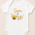 A white baby onesie with a yellow bee and the text "Sam is one" printed on it.