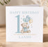 A birthday card with a teddy bear and balloons, celebrating a first birthday.