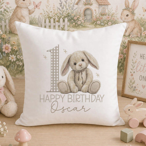 A white pillow with a cartoon rabbit and the number 1, along with the text "Happy Birthday Oscar", is displayed on a wooden surface.
