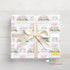 A gift box with a white ribbon and a personalized name printed on it, featuring a repeating pattern of unicorn illustrations and rainbows.