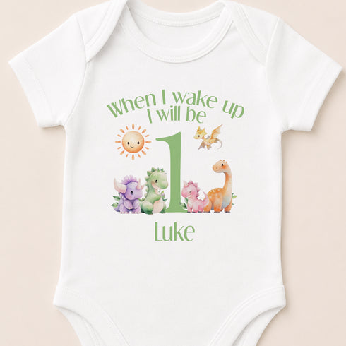 A white baby onesie with a personalized message and illustrations of various animals, including a sun, dragon, and dinosaur.