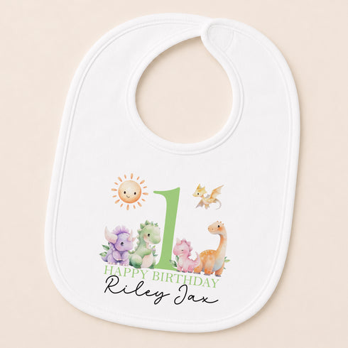 A white baby bib with a printed design featuring a sun, a dragon, and various animals, along with the text "Happy Birthday Riley".