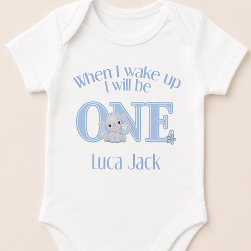 A white baby onesie with a blue elephant and text that says "When I wake up I will be one, Luca Jack".