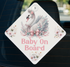 A diamond-shaped sign with a white background and a swan design, featuring a pink bow and flowers. The sign has the text "Baby On Board" written on it.