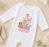A white onesie with a cartoon image of animals and the name "Ronnie" printed on it, along with a pink balloon.
