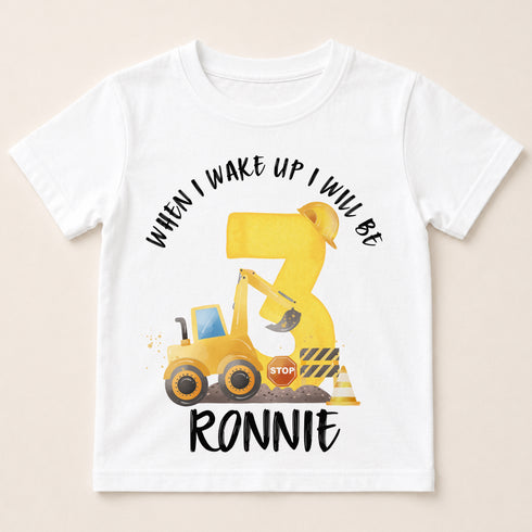 A white t-shirt with a graphic design featuring a yellow construction vehicle and the text "When I wake up I will be 3 Ronnie".