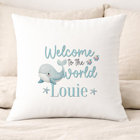 A white pillow with a cartoon image of a whale and the text "Welcome to the world" and "Louie" printed on it.