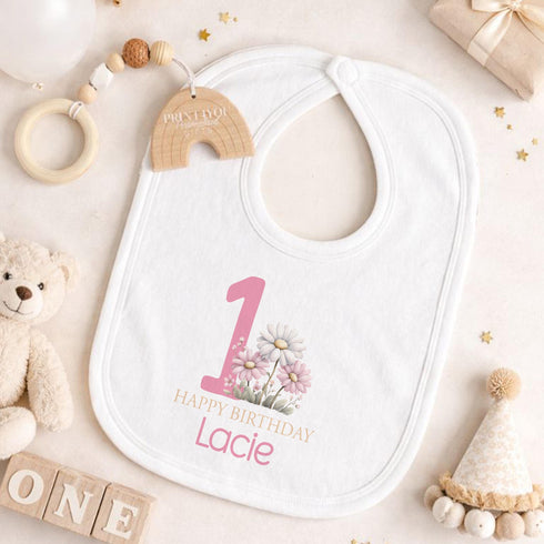 Personalised 1st birthday girl outfit with pink number 1, pretty daisy flower design, happy birthday text and custom name, shown on bib, vest, t-shirt, pyjamas and sleepsuit.