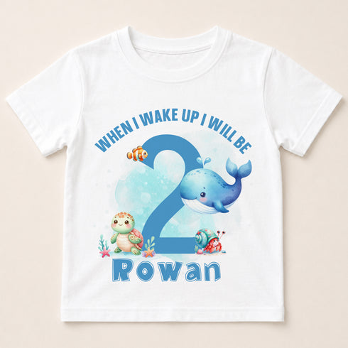 A white t-shirt with a design featuring a blue whale, a turtle, and other marine life, along with the text "When I wake up I will be 2 Rowan".