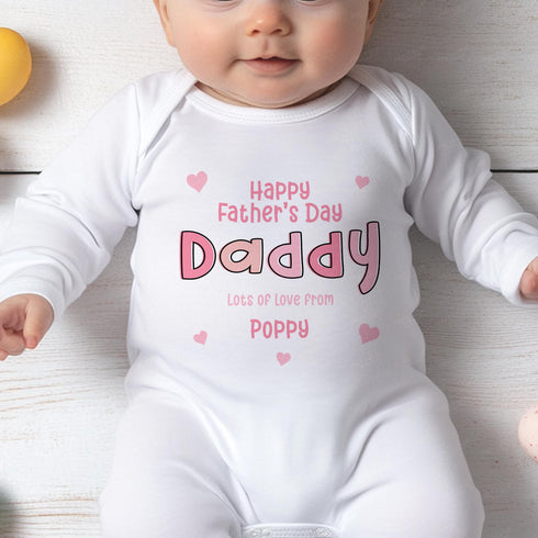 This photo shows a baby wearing a white onesie with a personalised Father's Day message. The text reads: "Happy Father's Day Daddy Lots of love from Poppy", written in pink, with small pink heart designs. It's a sweet and heartfelt tribute, perfect for celebrating Father's Day with a personal touch.