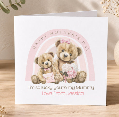 A greeting card with a pink and white color scheme, featuring two teddy bears sitting together and holding flowers. The card has a message that reads "Happy Mother's Day" and "I'm so lucky you're my Mummy" along with the name "Love from Jessica".