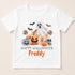 A white t-shirt with a Halloween-themed graphic design featuring a ghost, pumpkins, a skeleton, and bats. The text below the graphic says "Happy Halloween Freddy".