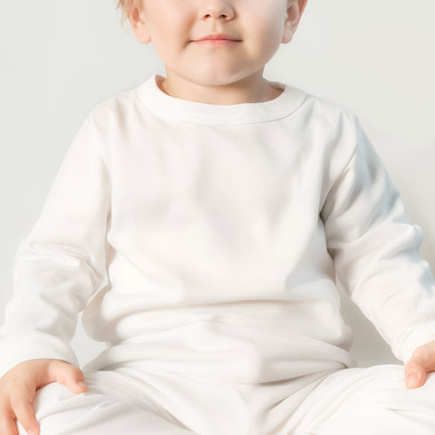 a little boy sitting on the floor wearing a white outfit