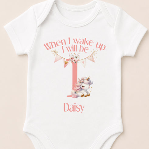 A white onesie with a pink unicorn and the text "When I wake up I will be up" printed on it.