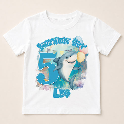 A white t-shirt with a graphic design featuring a shark and the number 5, along with the text "Birthday Boy Leo" and "5".