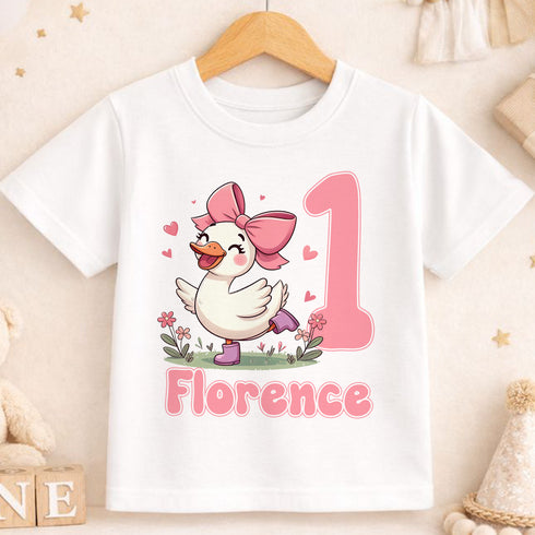 A white t-shirt with a cartoon image of a duck wearing a pink bow and surrounded by flowers, with the number 1 and the name "Florence" printed on it.