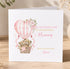 A white greeting card with a pink and white design featuring two teddy bears in a basket, an air balloon, and flowers. The card has a message that reads "Happy Mother's Day to my beautiful Mummy with lots of love Annie".