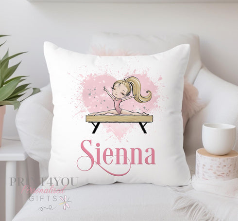 A blonde gymnast doing the splits on a wooden beam with a pink pink splashy heaty behind her and personalised with a pink swirly name. The design is printed on to an off white polyester cushion cover