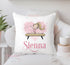 A blonde gymnast doing the splits on a wooden beam with a pink pink splashy heaty behind her and personalised with a pink swirly name. The design is printed on to an off white polyester cushion cover