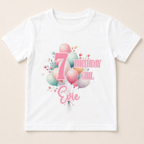 A white t-shirt with a graphic design featuring balloons and the number 7, along with the text "7 BIRTHDAY GIRL Evie" printed on it.