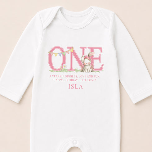 A white onesie with a pink text and an illustration of a rabbit on it.