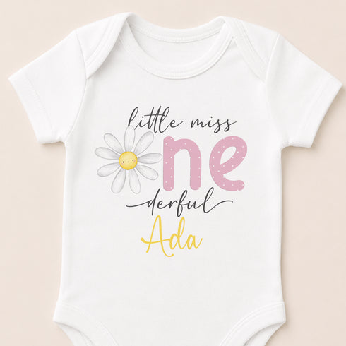A white baby onesie with a flower design and text printed on it.