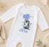 A white onesie with a penguin design and the number 1, along with the text "Alfie" printed on it, is displayed on a beige surface.