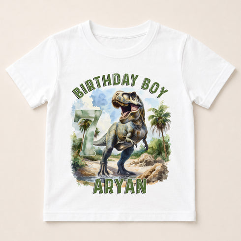 A white t-shirt with a graphic design featuring a dinosaur, specifically a T-Rex, and the text "BIRTHDAY BOY ARYAN" printed on it.