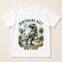 A white t-shirt with a graphic design featuring a dinosaur, specifically a T-Rex, and the text "BIRTHDAY BOY ARYAN" printed on it.