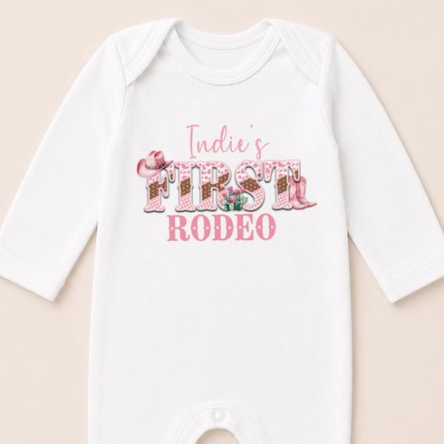 A white baby onesie with the text "Indie's FIRST RODEO" printed on it.