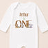 A white onesie with the text "Arthur is ONE" and illustrations of a lion, zebra, and elephant.