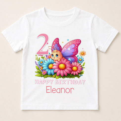 A white t-shirt with a colorful graphic design featuring a butterfly surrounded by flowers and the number "2" in pink.