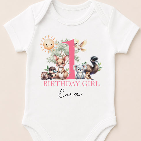 A white baby onesie with a pink and green animal print and the text "BIRTHDAY GIRL Eva" printed on it.