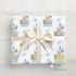 A gift box with a white ribbon and a pattern of blue and white elephants, giraffes, and other animals.