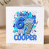 A birthday card with a colorful design featuring the text "I WAS 6 NOW I'M COOPER" surrounded by various shapes and patterns in shades of blue and black.