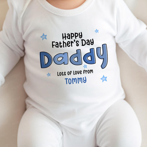 A baby wearing a white onesie with a printed Father's Day message that reads: 'Happy Father's Day Daddy, Lots of love from Tommy.' The text uses a playful font style and is decorated with blue stars. This design adds a personal, heartfelt touch to the gift, perfect for celebrating Father's Day