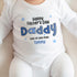 A baby wearing a white onesie with a printed Father's Day message that reads: 'Happy Father's Day Daddy, Lots of love from Tommy.' The text uses a playful font style and is decorated with blue stars. This design adds a personal, heartfelt touch to the gift, perfect for celebrating Father's Day